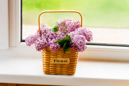 decorative flower basket with branches of spring lilacs on the windowsill of a country house. the concept of a good spring moodの写真素材
