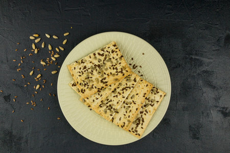 whole grain crispy cookies on a white plate with sesame and flax seeds. close-up. black background