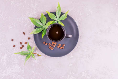 a dark cup with aromatic coffee and connabis leaves on a plate stands on a gray concrete background. The concept of morning coffee for energyの写真素材