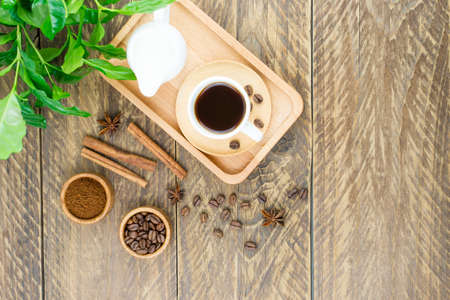 a cup of aromatic coffee and a milkman with milk on a tray. morning breakfast .green arabica coffee leaves on a wooden backgroundの写真素材