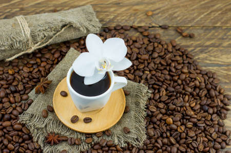 a cup of freshly prepared aromatic coffee on a wooden table with an orchid flower and coffee beans. composition of morning coffee in the countrysideの写真素材