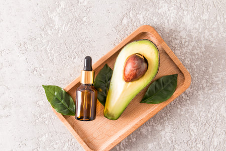 whey or cosmetic avocado oil in a cosmetic bottle on a wooden tray with ripe avocado. natural...