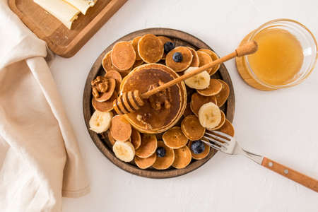 Original trend breakfast on a large wooden round tray. assortment of pancakes with honey, banana and nuts. top viewの写真素材
