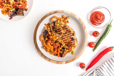 top view of a plate of roasted chicken breast steak and roasted vegetables. sauce in a bowl. pepper....