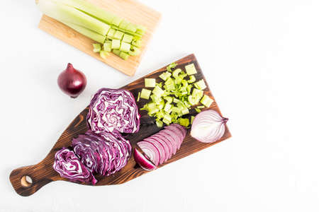top view of the kitchen wooden board with chopped red cabbage, purple onions, a stalk of fresh celery. white background.の写真素材