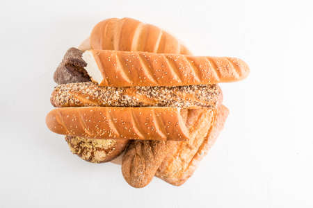 an assortment of fresh crispy bread on a wooden round board. top view. white background.の写真素材