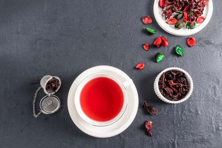top view of a white cup with a saucer of fragrant hibiscus rose tea. dry rose leaves in the bowl. black background. natural antiseptic vitaminsの写真素材