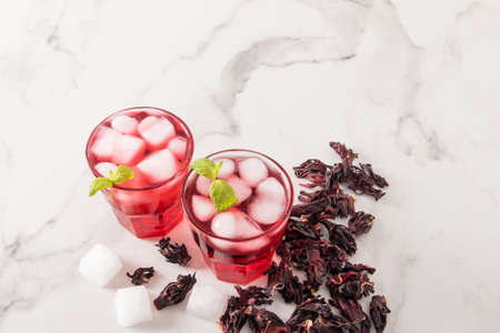 a cold drink made from hibiscus rose petals with ice cubes and mint on a marble table and dry rosebudsの写真素材