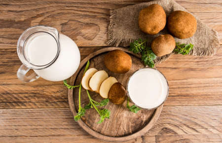 top view of potato vegetable milk in a jug and glass, chopped potato slices, leaves, tubers on a wooden tableの写真素材