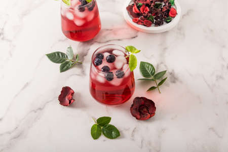 tonic vitamin drink from rose petals hibiscus with blueberries, mint leaves, ice cubes in glasses on a marble table. iced teaの写真素材