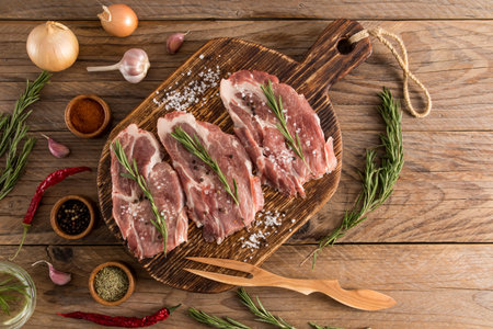 three steaks of farm pork on a wooden rustic cooking board with ingredients for cooking. top view....