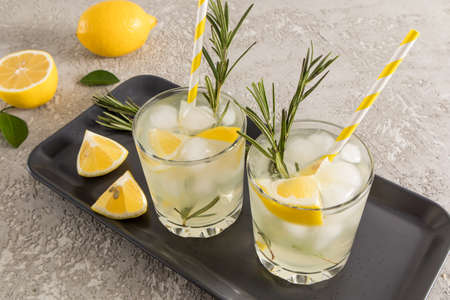 two glasses of citrus fruit vitamin water on a dark ceramic tray with lemon slices and rosemary. detox water.の写真素材