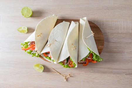 top view of four wrapped buritto with vegetables and chicken fillet on a wooden board and kitchen...