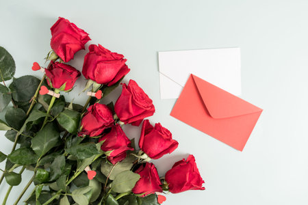 bouquet of red fresh roses and two greeting envelopes on a white background. top view