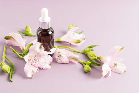 moisturizing liquid oil for the face, a cosmetic natural product in a bottle with a pipette made of glass a background of flowers alstroemeriaeの写真素材