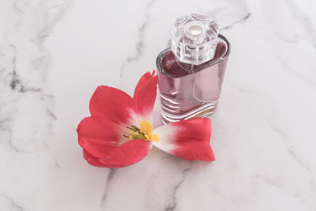 cosmetic perfume spray or eau de toilette in a glass transparent bottle on a marble white background and petals of a spring flower. space for text.の写真素材