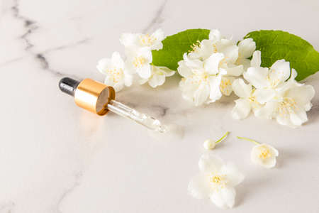a pipette filled with natural jasmine oil lies on a marble white table with fragrant flowers. a copy of the space.の写真素材