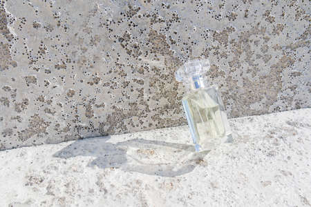 a luxurious perfume bottle on a gray concrete background is tilted on a cement slab in the rays of the sun. modern presentation of a cosmetic product.の写真素材