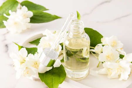 an open bottle with a dropper of cosmetic organic jasmine oil on a background of flowers for face and body skin care. relaxation. phytotherapy.の写真素材