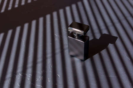 a luxurious black matte bottle of men's perfume water against a background of parallel strips of shadows. advertising concept of men's perfumesの写真素材