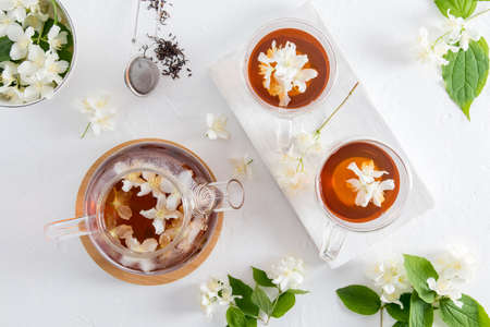 top view of a glass teapot with healing herbal jasmine tea and two glass cups of tea on a white wooden board. drink rich in vitamins and mineralsの写真素材
