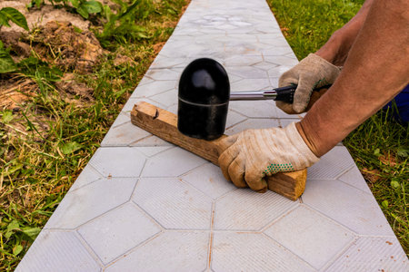 the hands of a professional worker hit the slab with a special rubber hammer in the process of laying a garden path made of stone tilesの写真素材