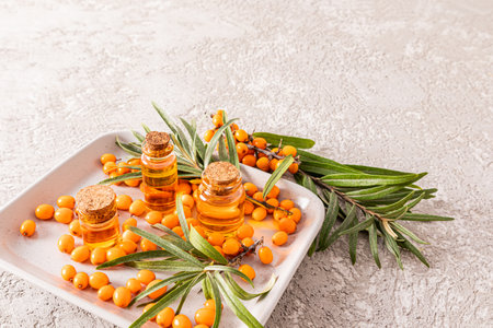 three different glass bottles of sea buckthorn oil on a gray ceramic rectangular plate with berries and leaves. gray background. a natural remedyの写真素材