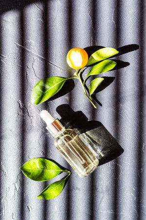 serum for the face in a glass bottle with a dropper on a dark background in the rays of the sun and citrus . top viewの写真素材