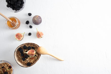 top view of the bowl with homemade granola or muesli, with figs and blackberries, a jar of honey . white background. a copy of the spaceの写真素材
