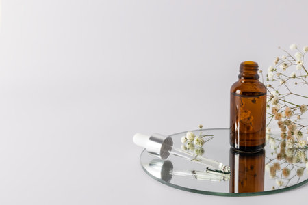 an open bottle with natural cosmetic oil or a serum for organic skin care stands on a round mirror with a filled pipette. a copy space.の写真素材