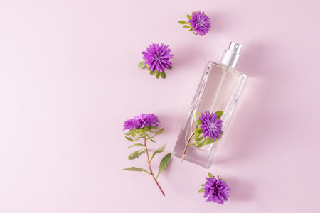 a glass perfume bottle and a flat floral arrangement on a pink background. top view. advertising...