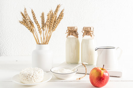 front view of two bottles and a jug of milk, cottage cheese, sour cream in bowls. a vase with ears of corn. the concept of the holiday of Shavuotの写真素材