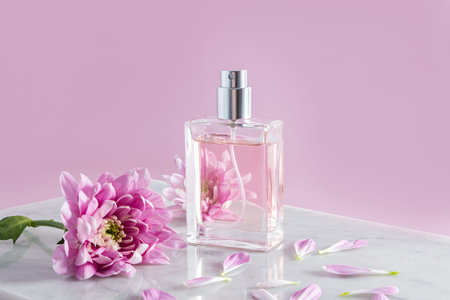an elegant bottle of womens perfume or spray stands on part of a white marble podium and a pink...