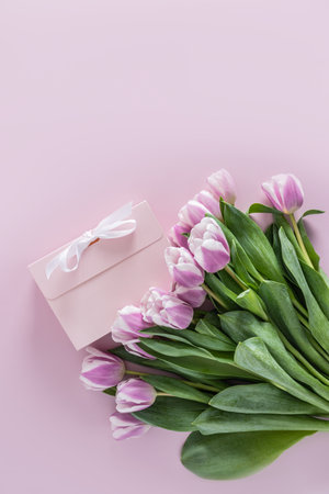 beautiful spring bouquet of tulips on a purple background with a gift box with a white ribbon. vertical view. space for textの写真素材