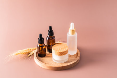 Three different cosmetic bottles with a dropper with an organic natural remedy and a jar of cream on a wooden round tray and a beige backgroundの写真素材