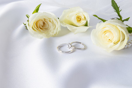 Wedding arrangement with two wedding rings made of platinum with diamonds and delicate tea roses on a white satin background. layout for designの写真素材