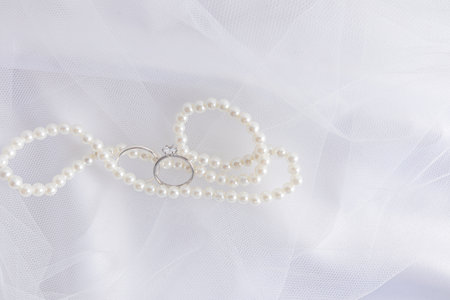 A chic background for wedding design. An elegant white pearl necklace and two white gold diamond engagement ringsの写真素材