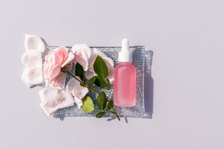 Cosmetic, serum in a white matte bottle for face and body skin care lies on a glass plate. gray background .copy space. rose. pink petals. top view.の写真素材