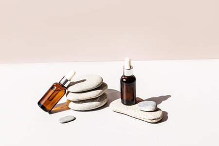 Two cosmetic bottles made of amber glass with a pipette with organic cosmetics to moisturize the skin against the background of sea oval stonesの写真素材