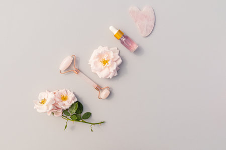 quartz roller, gua sha scraper, cosmetic bottle with rose oil or serum for face and neck skin care and massage. top view. flat layout.の写真素材