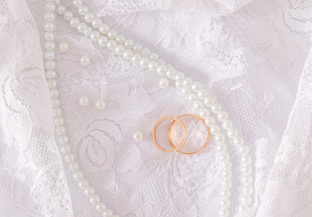 Two gold wedding rings lie on a luxurious vintage part of the bride's wedding dress with a string of pearl beads. Wedding concept. Top view.の写真素材