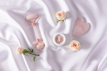 Set of cosmetics and tools on white satin background with live rosebuds. Top view. Cosmetic massage. home care.の写真素材