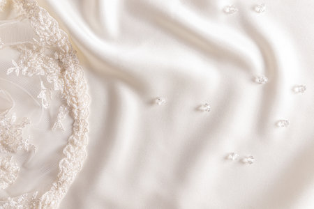 Delicate beige satin background with glass transparent beads and part of lace, embroidery with beads, sequins. A copy space. Wedding design mockup.の写真素材