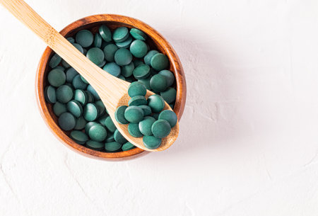 Close-up of green tablets of beneficial spirulina seaweed on a wooden spoon in a wooden bowl filled with tablets. Top view. Detoxの写真素材
