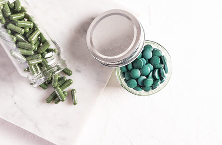 Round blue-green natural spirulina algae tablets in bank glass on white background. medical jar with...