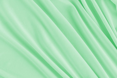 Luxury holiday textiles. Satin delicate background. Soft waves of - green colored satin fabric. A...