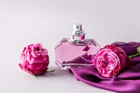 Glass elegant bottle of women's perfume among delicate rose buds and women's accessory chiffon purple scarf. Presentation of the fragranceの写真素材