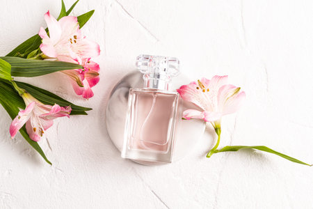 A chic bottle of women's perfume lies on a round marble podium and a white background with delicate...