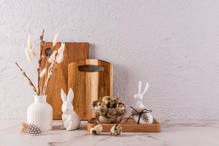 Stylish eco-friendly background for Easter holiday with ceramic Easter rabbit figurines, vase with willow twigs, bowl with quail eggsの写真素材