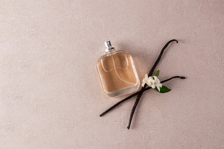 Glass bottle of perfume or cosmetic spray with natural vanilla scent on beige stone background with vanilla sticks. Top view. A copy spaceの写真素材